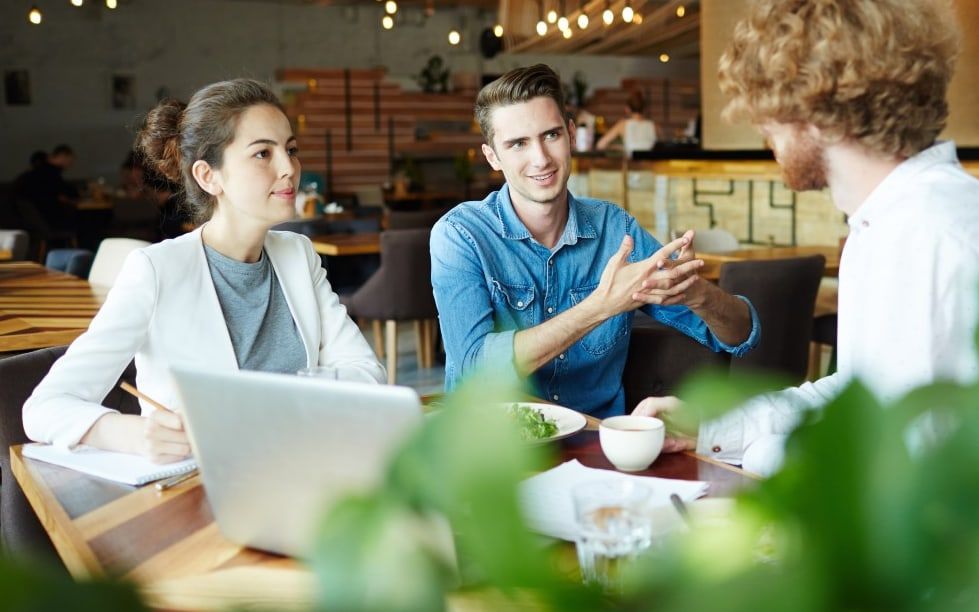 Three colleagues working together over a laptop in a bright café-style workspace.