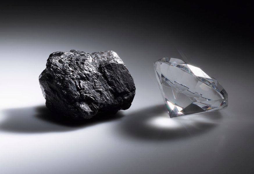 A lump of coal beside a cut diamond, lit against a dark ground.